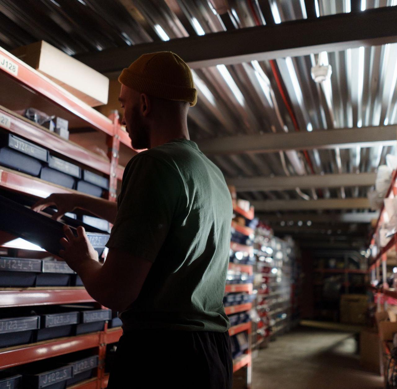 A man organizing inventory on shelves in a dimly lit warehouse, wearing a uniform.