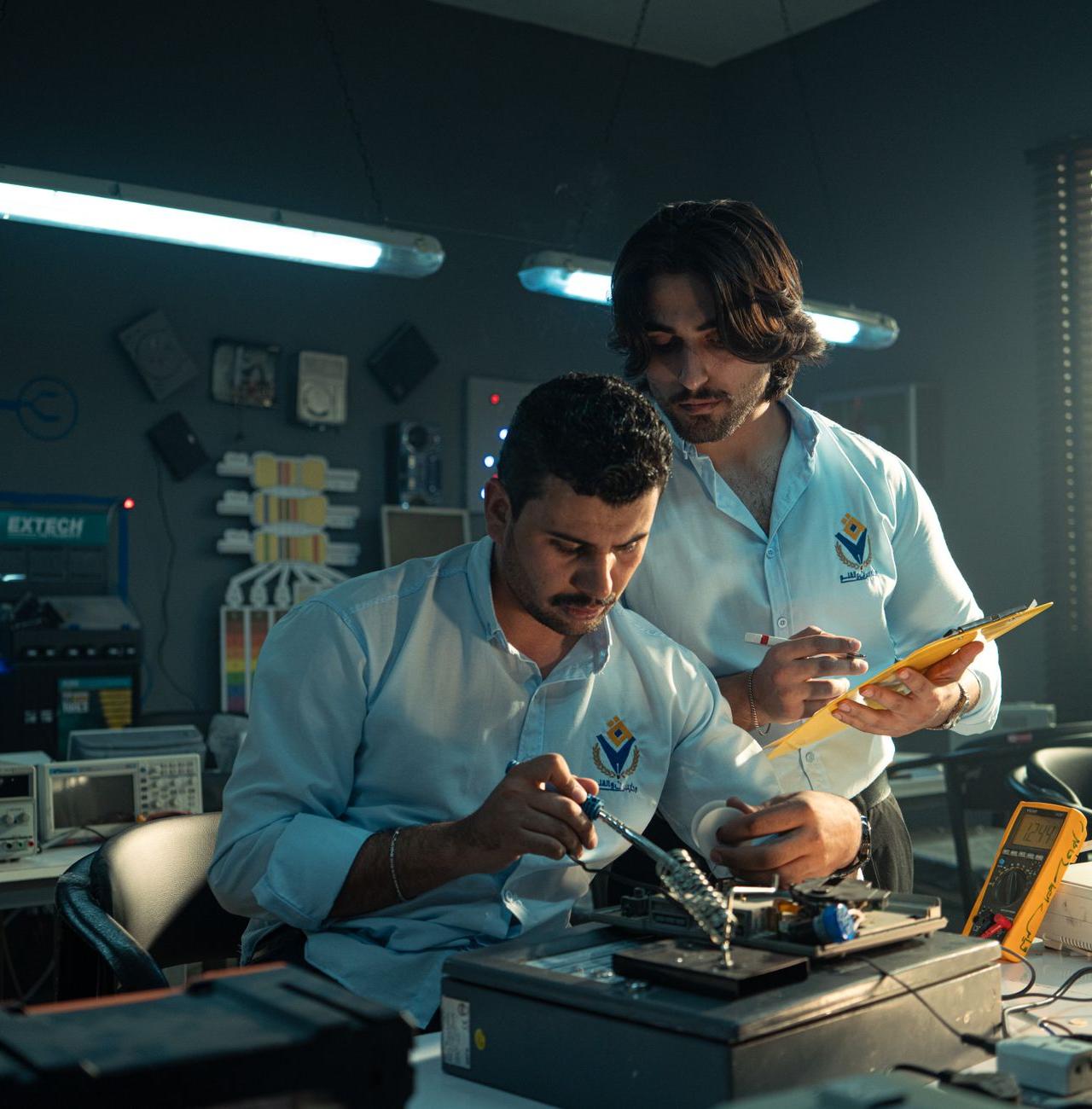 Two men working on an electronics project in a Baghdad lab, focused and collaborating.