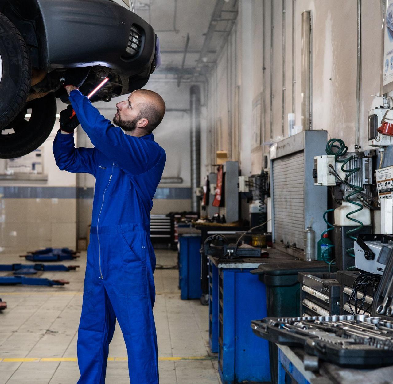 Mechanic inspecting a raised car in an auto workshop for maintenance and repair services.