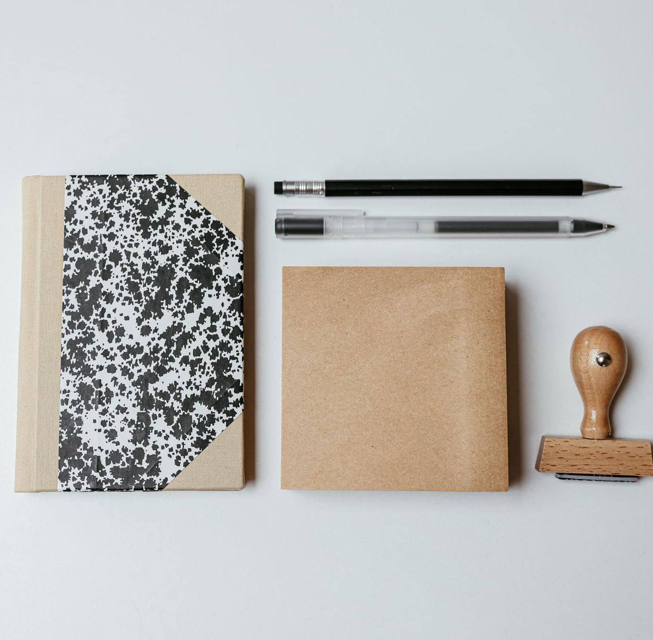 A modern flatlay featuring a notepad, pens, and a wooden stamp on a clean background.
