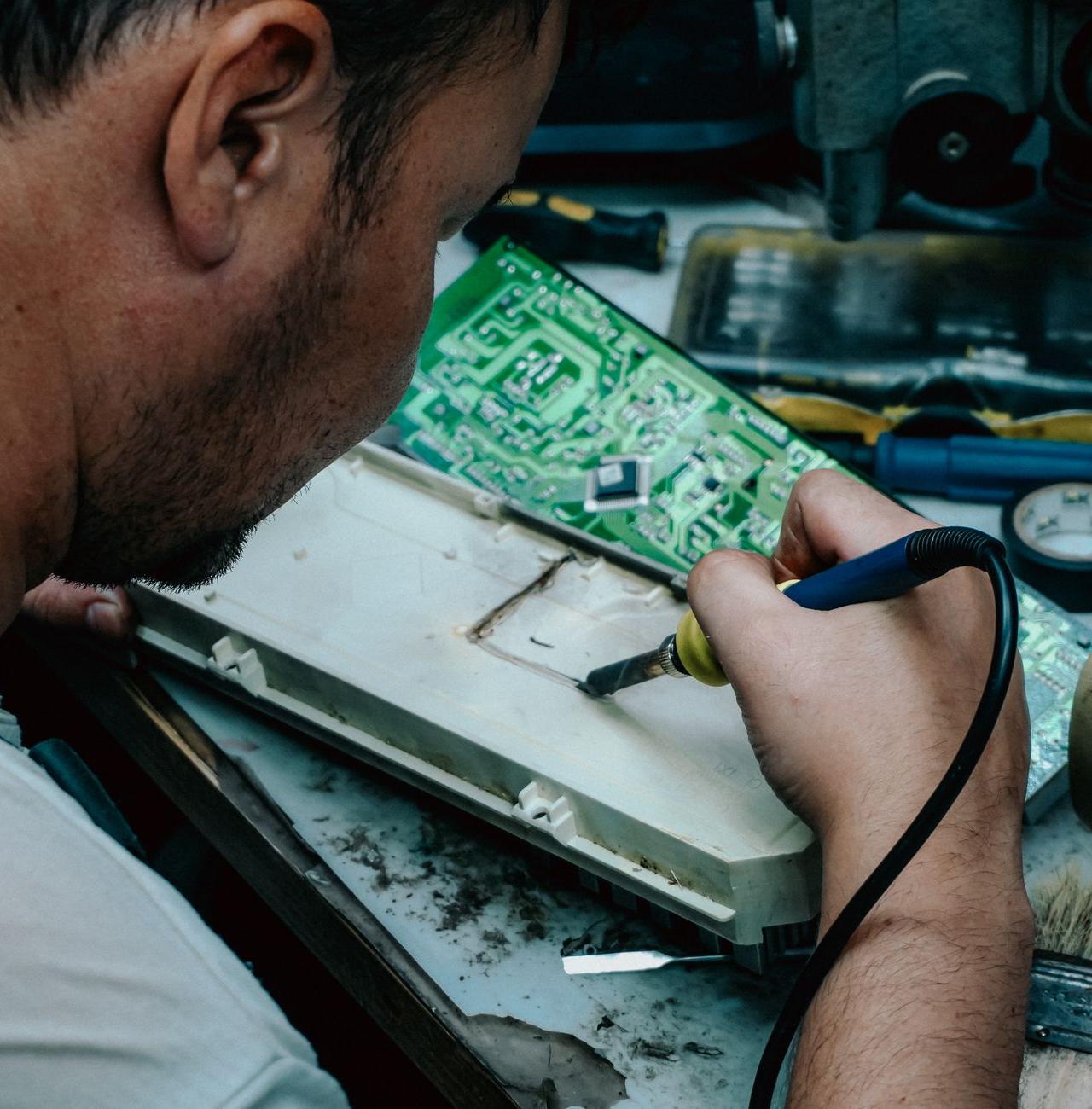 A focused technician using a soldering iron to repair electronic components at a workstation.