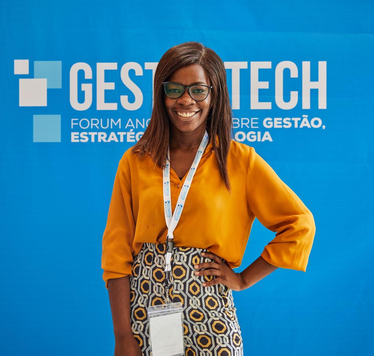 Smiling woman in orange blouse poses confidently at Gest Tech event backdrop.