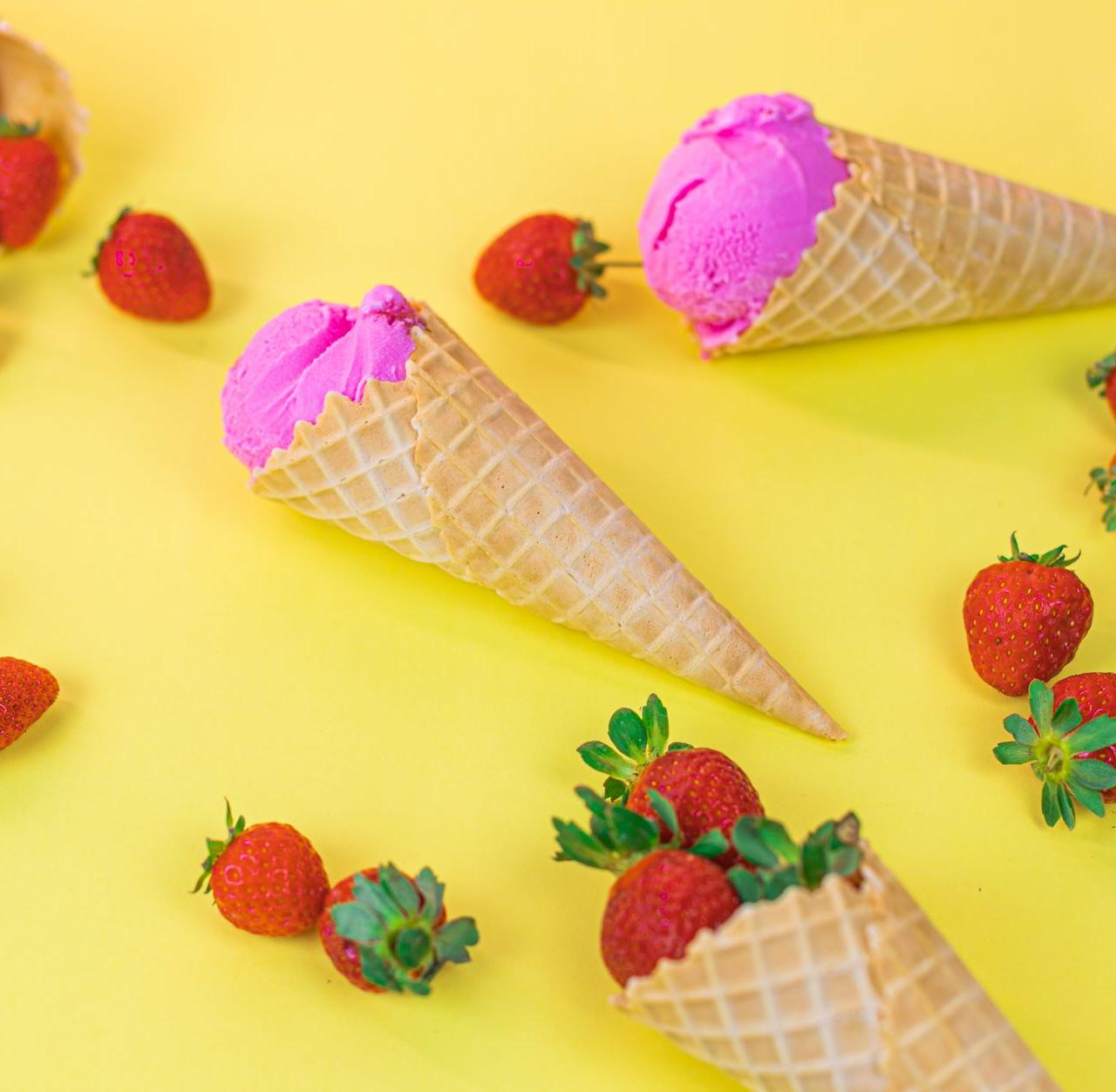 Colorful ice cream cones with strawberries on a bright yellow background. Perfect summer treat.