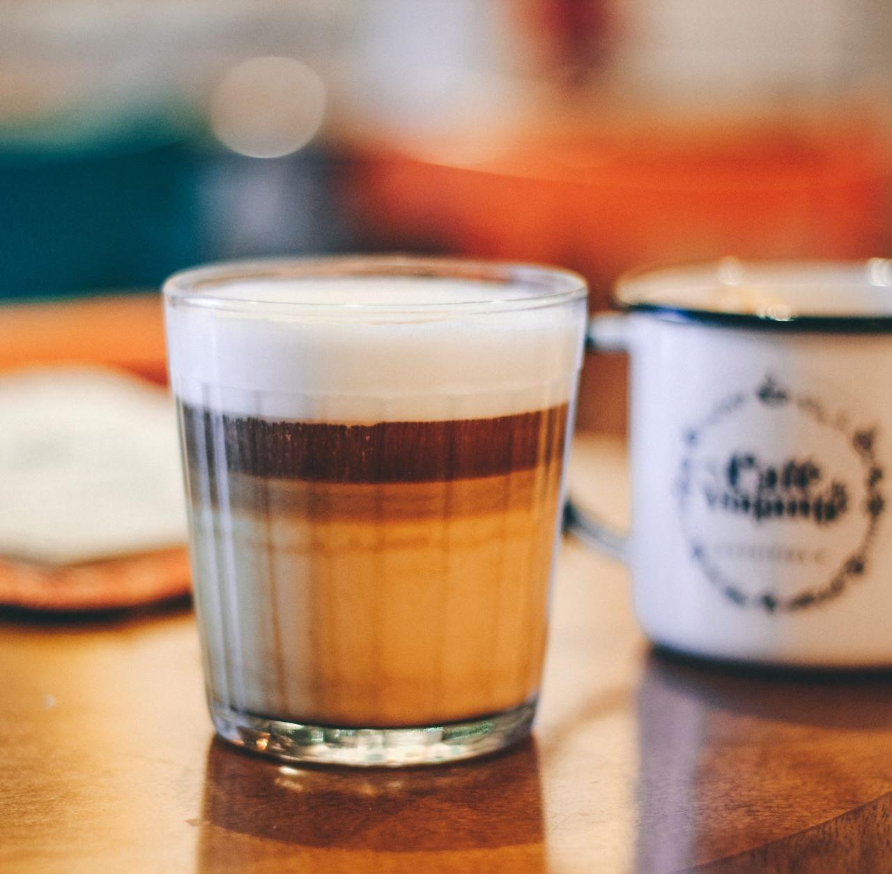 A creamy latte macchiato and vintage mug on a cozy wooden table in a cafe setting.