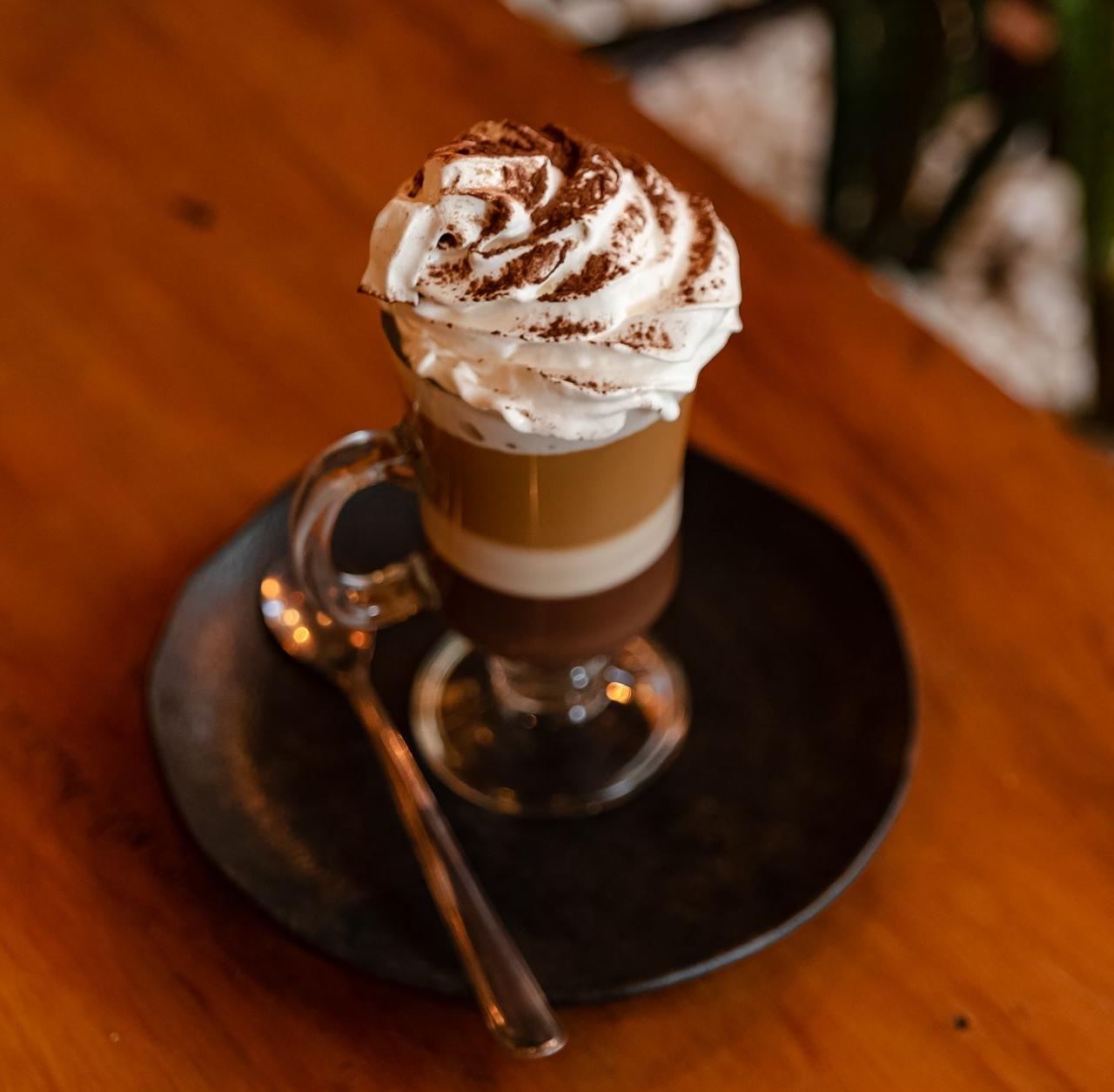 A close-up of a layered coffee topped with whipped cream served on a dark plate.