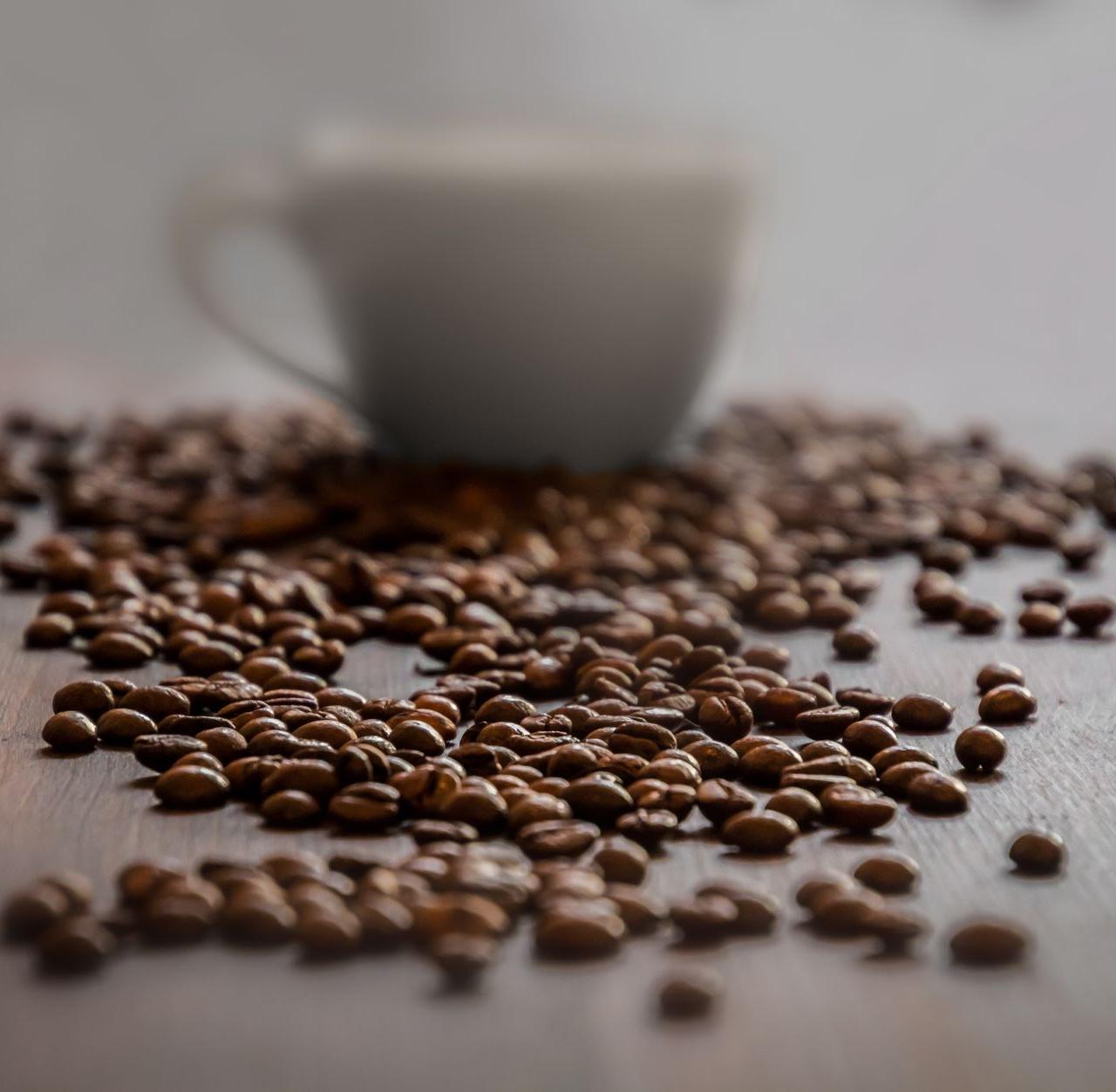 Close-up of coffee beans scattered around a cup on a wooden table.
